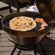 The RT-B380 Bullseye wood pellet grill with it's lid open and grilling a pizza and chicken breasts.