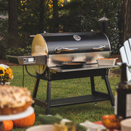 The RT-1250 wood pellet grill in the backyard with the front folding shelf out with a cast iron skillet and a casserole dish on the front folding shelf.
