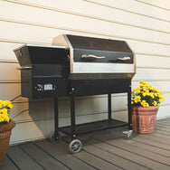 The RT-590 wood pellet grill set to 350°F on a back porch next to two yellow flowers in pots. 