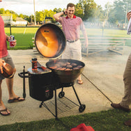 The RT-B380 Bullseye at a tailgate setting with multiple people around it and it is turned up to 500°F with burgers and hotdogs being grilled. 