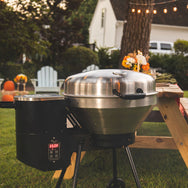 The RT-B380 Bullseye wood pellet grill in a backyard and turned up to 350°F with an elegantly set picnic table behind it. 