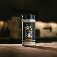 Chef Greg's Four Letter Rub All Purpose Deliciousness in bottle with faded kitchen background behind.