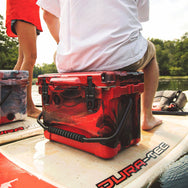 Guy sitting on top of the 20 qt Red and Black RECTEQ ICER while floating down the river on a paddle board. 