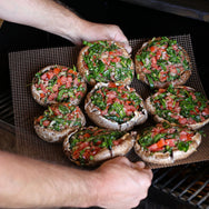 Heavy duty Teflon-coated fiberglass mesh cooking mat coming off the grill with stuffed bruschetta mushrooms. 
